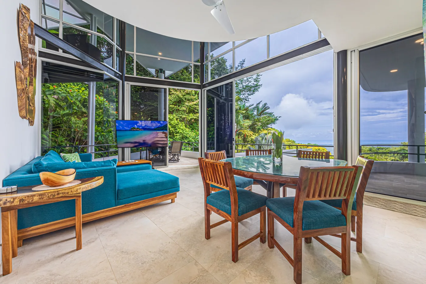 Sala con ventanales de piso a techo, un sofá seccional turquesa y una mesa de comedor con vista al mar
