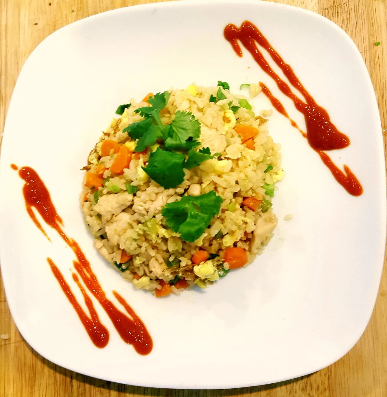 Fried rice plate with chicken, carrots, cilantro, and sriracha drizzle