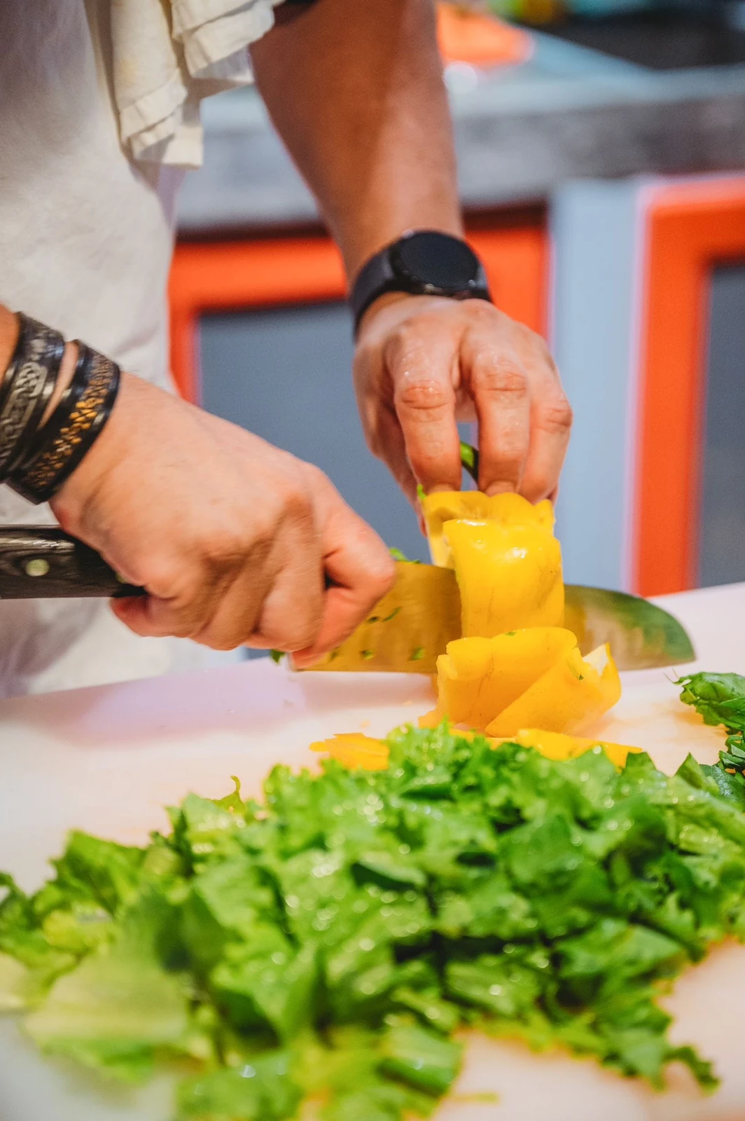 Close-up of hands slicing a yellow sweet pepper beside chopped greens