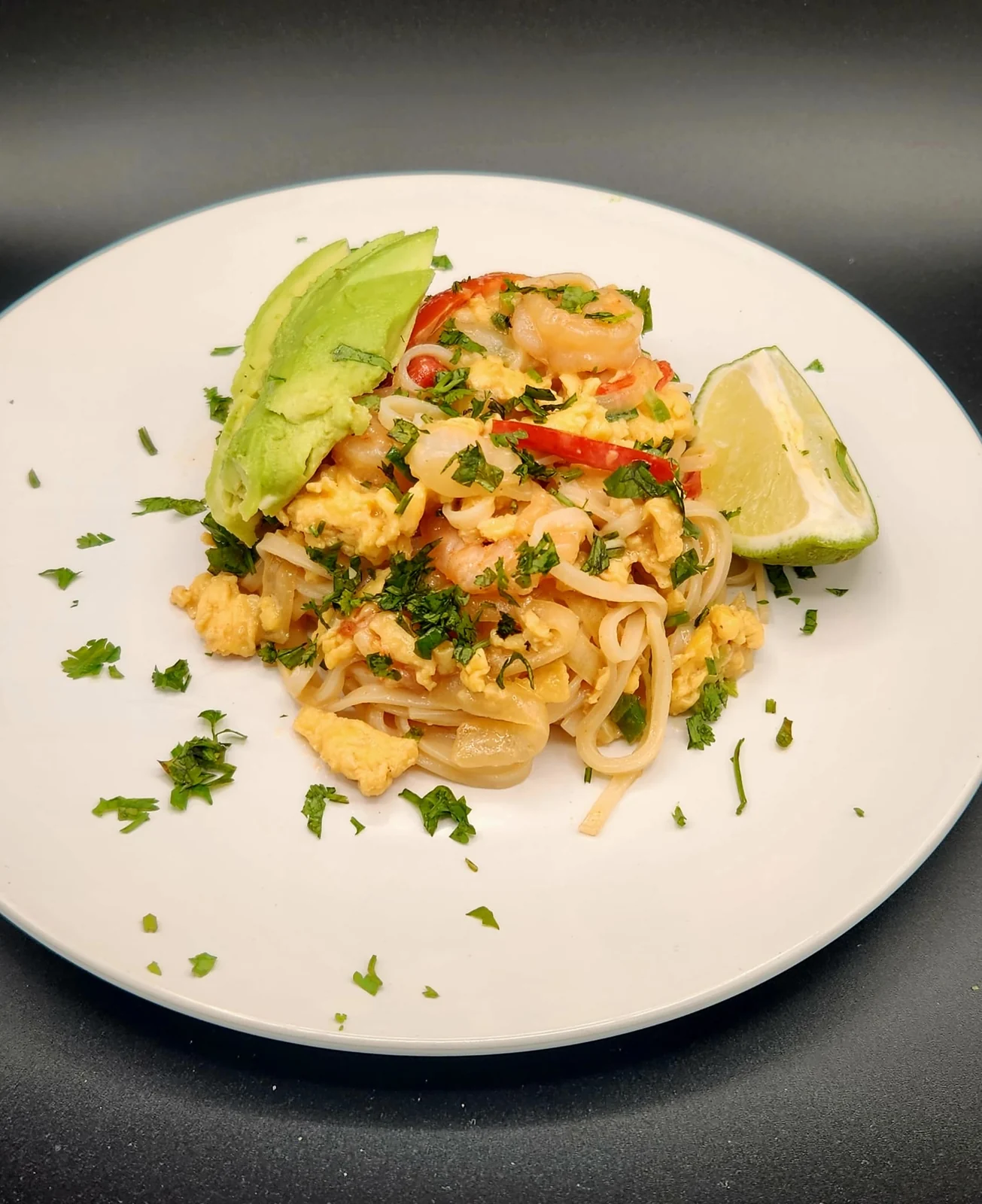 Shrimp and egg rice noodles garnished with cilantro, avocado, and lime