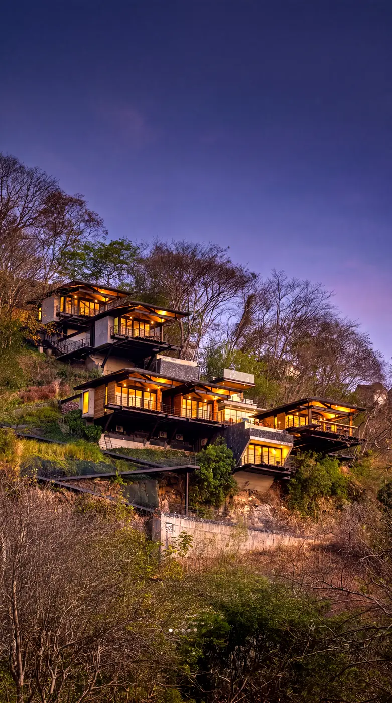The villas lit at dusk, stepped down the forested hillside
