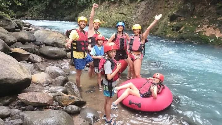 Family group in life jackets and helmets posing in a river during a tubing tour