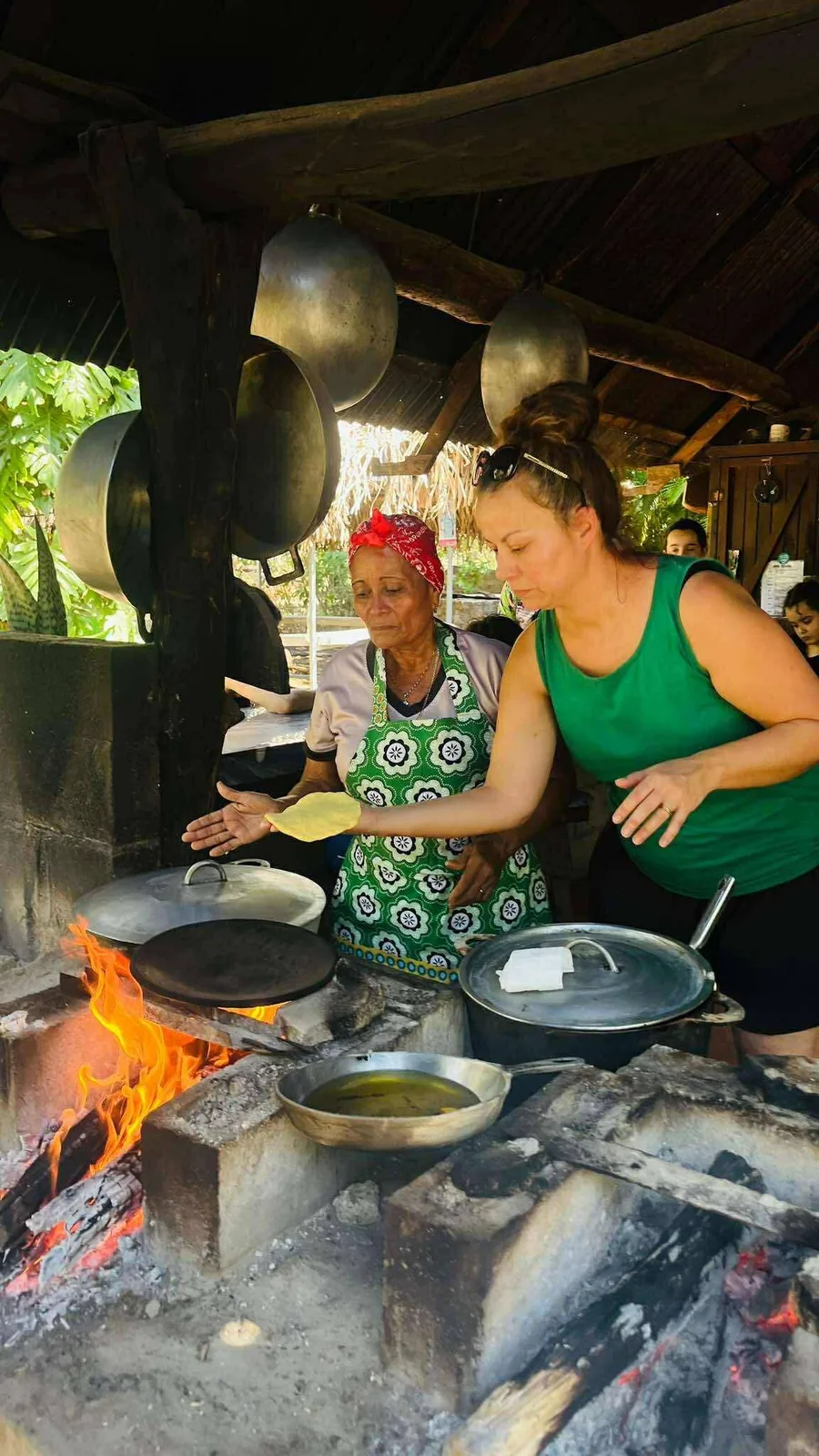 Woman learning to make tortillas over an open wood fire with a local cook